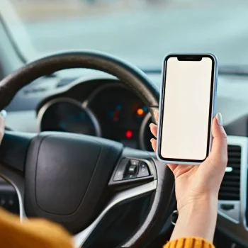 Digital marketing support for the automobile industry – driver holding a smartphone inside a modern car.